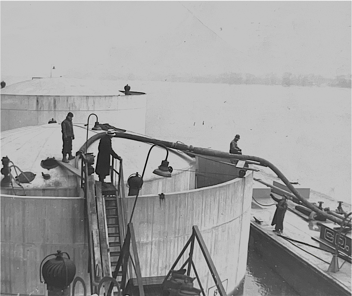 Men loading from a barge on the river into tanks.