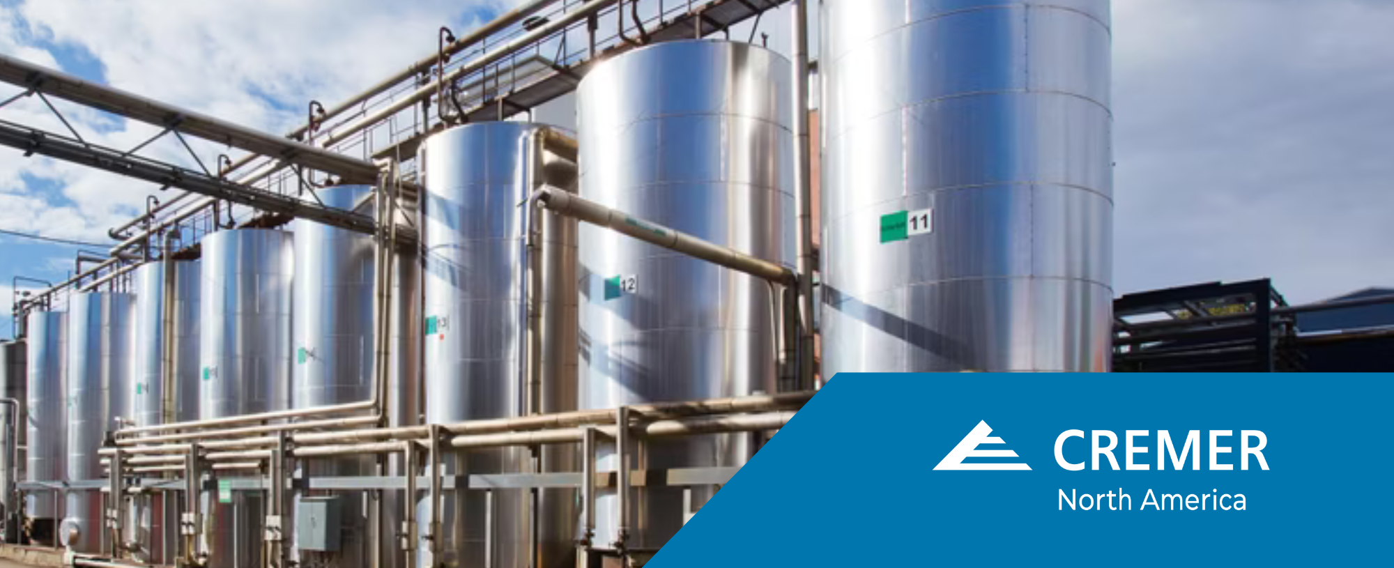 Multiple stainless steel storage tanks with industrial piping at a modern chemical processing plant, featuring CREMER North America branding.